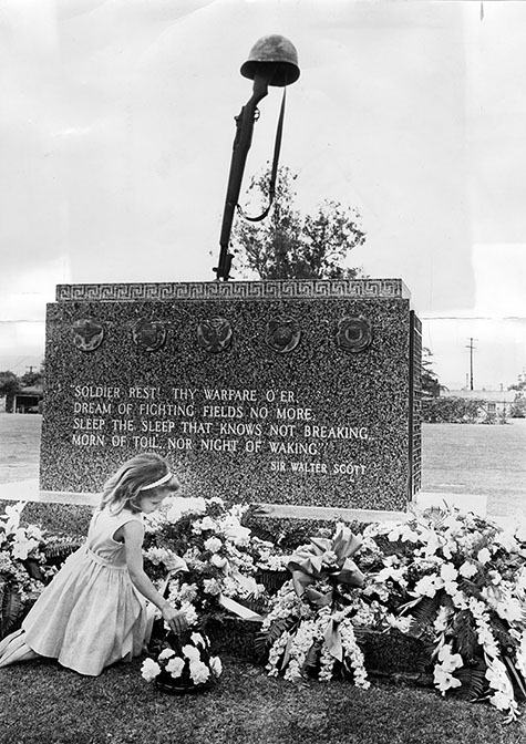 Seven-year-old Patricia Ross places flowers at the base of the monument in Valhalla Memorial Park, North Hollywood, honoring soldiers killed on battlefield.