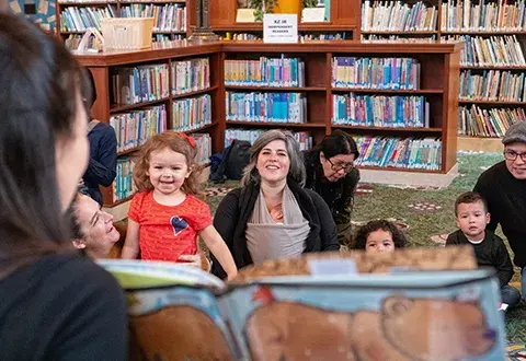 a librarian reads to a group of young kids and their caregivers