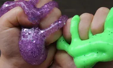 hands squishing purple glittery and green slime