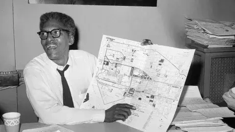 Bayard Rustin holding up a city map and pointing at it.