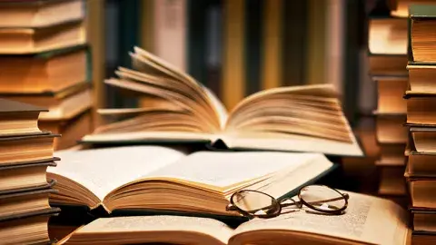 Three stacks of books surrounding three opened books, with a pair of glasses set on top.
